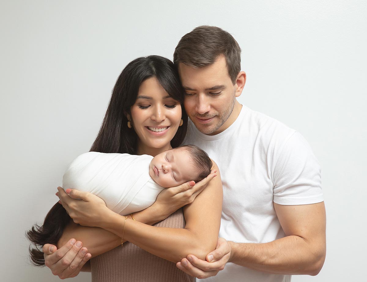 A married NYC couple holds their infant cradled in their arms.