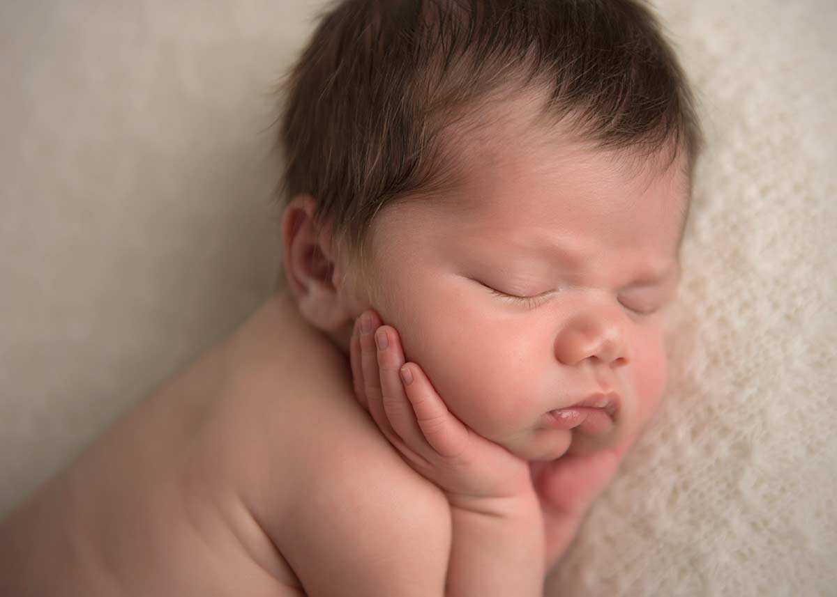 Sleeping baby with his hands underneath his cheeks.