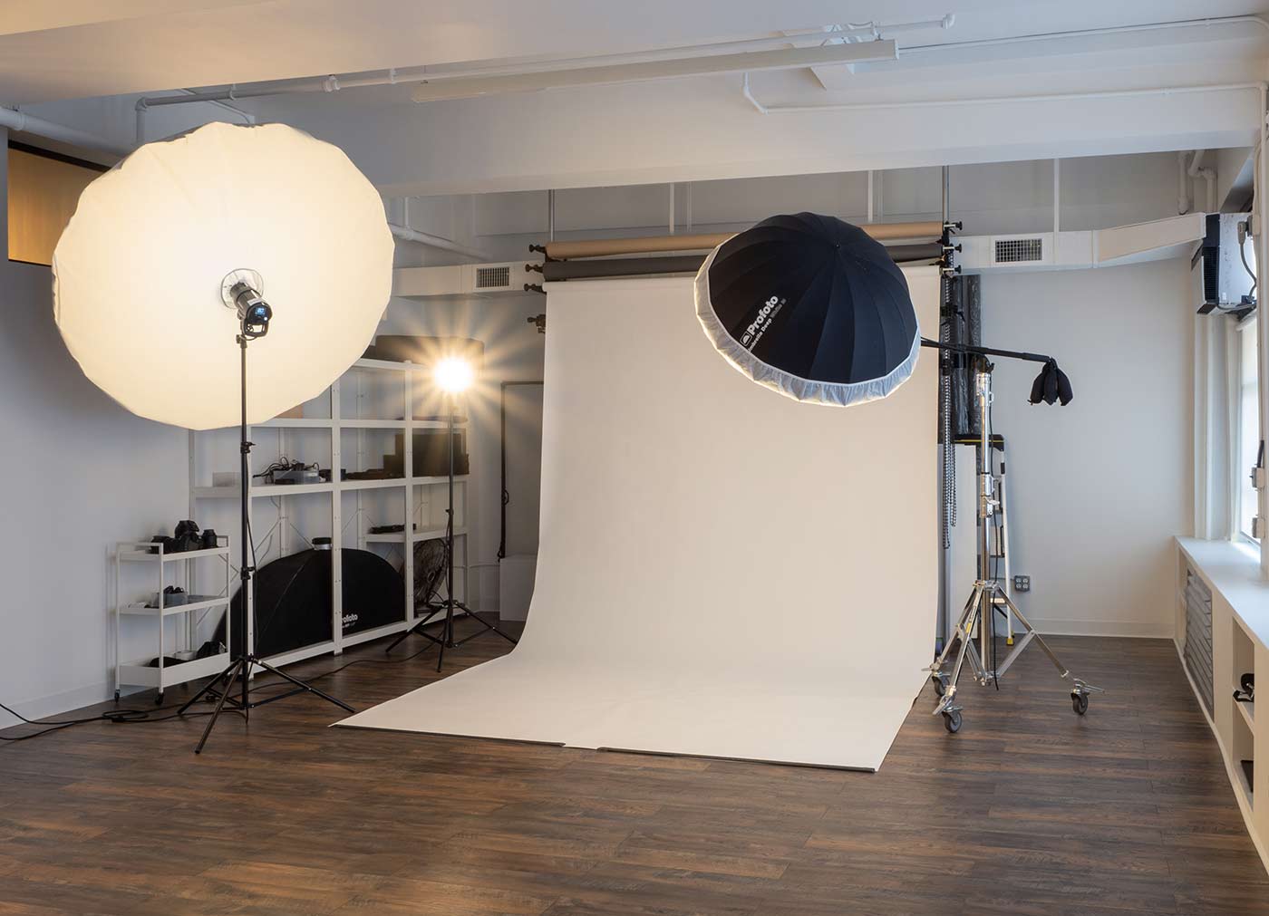 Interior of a NYC photography studio, showing a white seamless backdrop, and a variety of flash strobes mounted on stands.