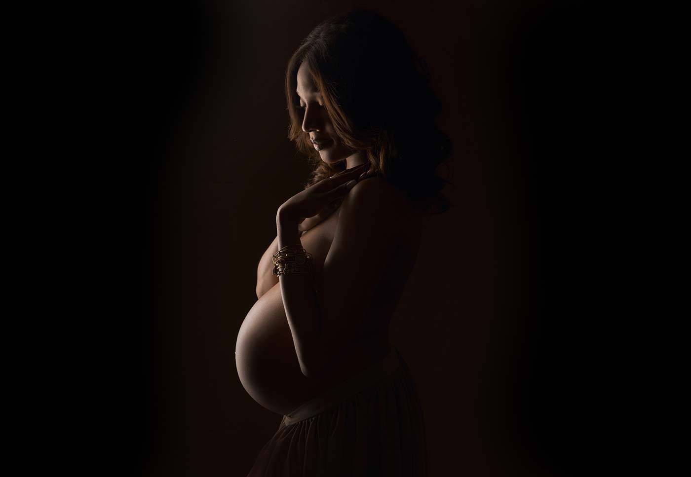 Silhouette of a pregnant woman. Her belly is tastefully lit, showing a crescent shape. Her eyes are closed and her expression is calm.