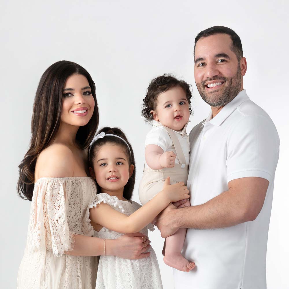 A modern photo portrait of a NYC family. Mother & father, holding their two young children. They're all dressed in off-white casual attire.