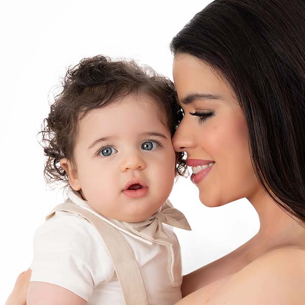 Closeup of a mother with long dark hair, nuzzling her baby son. The boy, with curly hair, is happy to be held and loved by his mother. The image was taken at a professional photo studio in NYC.