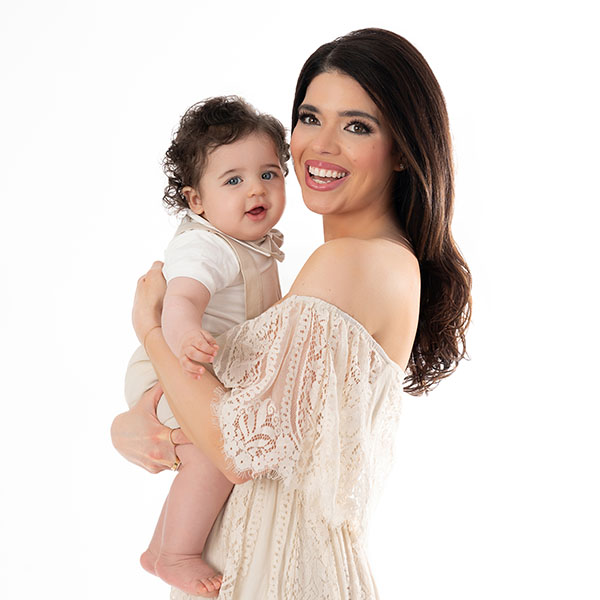 A stylish mother wearing a knit dress is posing for the camera while holding her adorable little son. The photo is indicative of a portrait taken at a NYC photography studio.